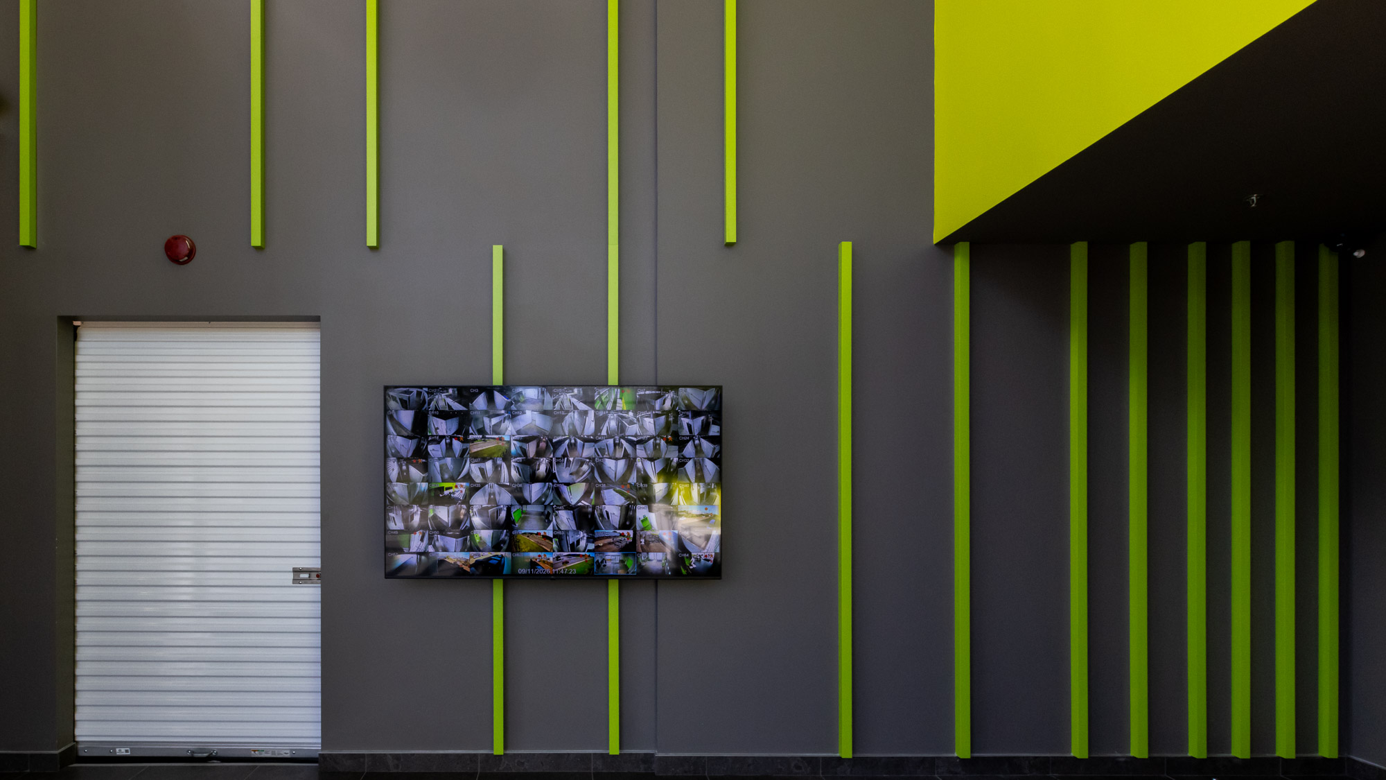 Mur intérieur gris avec bandes verticales vertes et écran d’information dans les installations Pandora Mini-Entrepôts.